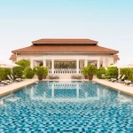 Symmetrical view of a luxury Singapore hotel pool with a distinctive colonial-style main building and terracotta roof. Perfect for high-end Singapore travel and holidays.