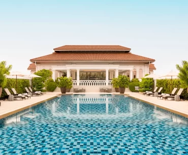 Symmetrical view of a luxury Singapore hotel pool with a distinctive colonial-style main building and terracotta roof. Perfect for high-end Singapore travel and holidays.