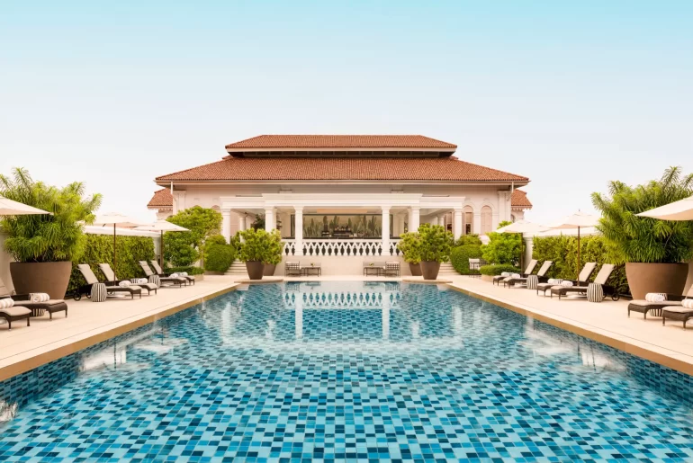 Symmetrical view of a luxury Singapore hotel pool with a distinctive colonial-style main building and terracotta roof. Perfect for high-end Singapore travel and holidays.