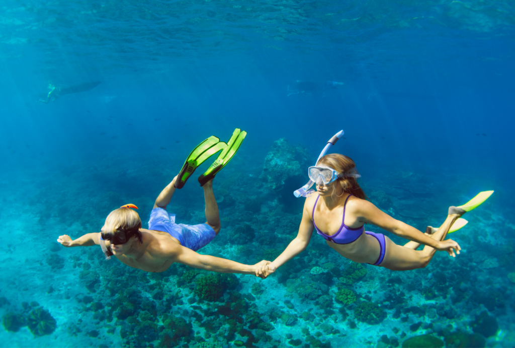  Young couple in swimsuits holding hands underwater, enjoying a free dive with snorkeling masks in the vibrant sea.