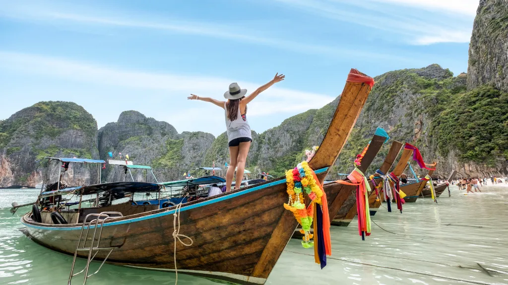 A woman on a luxury travel tour in Thailand, celebrating on a traditional longtail boat at a beautiful beach.