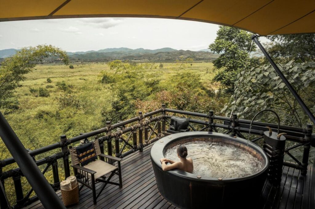 A woman relaxing in a private outdoor jacuzzi at a luxury resort in Thailand, overlooking a lush landscape.