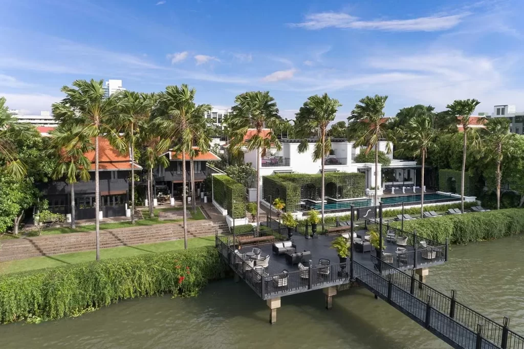 Aerial view of The Siam Hotel Bangkok on the banks of the Chao Phraya River, showing the riverside jetty terrace, pool, and palm-lined heritage compound — Bangkok's most private luxury boutique hotel