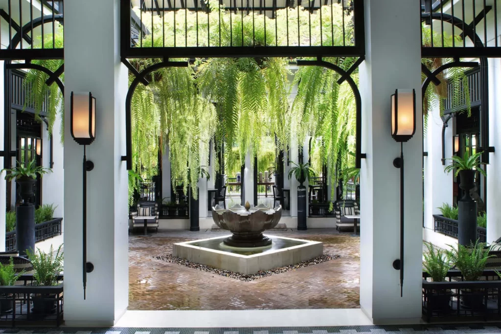 The open-air courtyard at The Siam Hotel Bangkok, with cascading ferns, a bronze lotus fountain, and Art Deco ironwork — one of Bangkok's most architecturally distinctive luxury boutique hotels