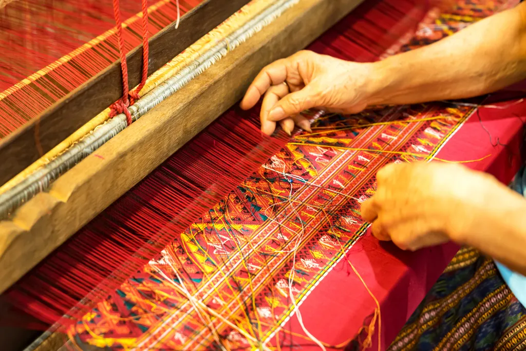 Artisan hands weaving traditional patterned silk on a wooden loom in Laos