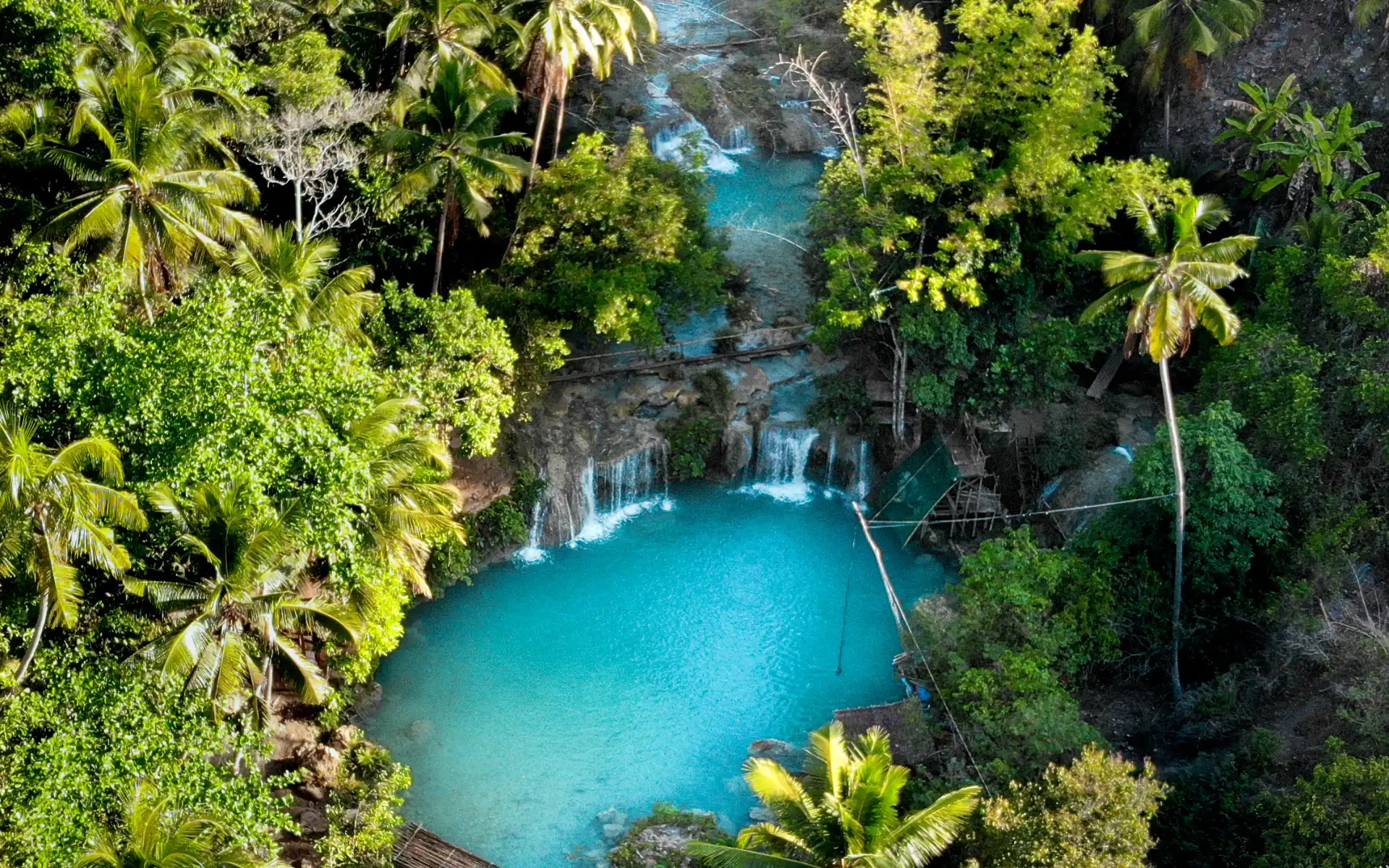 Aerial view of Cambugahay Falls, a tiered turquoise waterfall surrounded by lush tropical jungle in Siquijor, Philippines.
