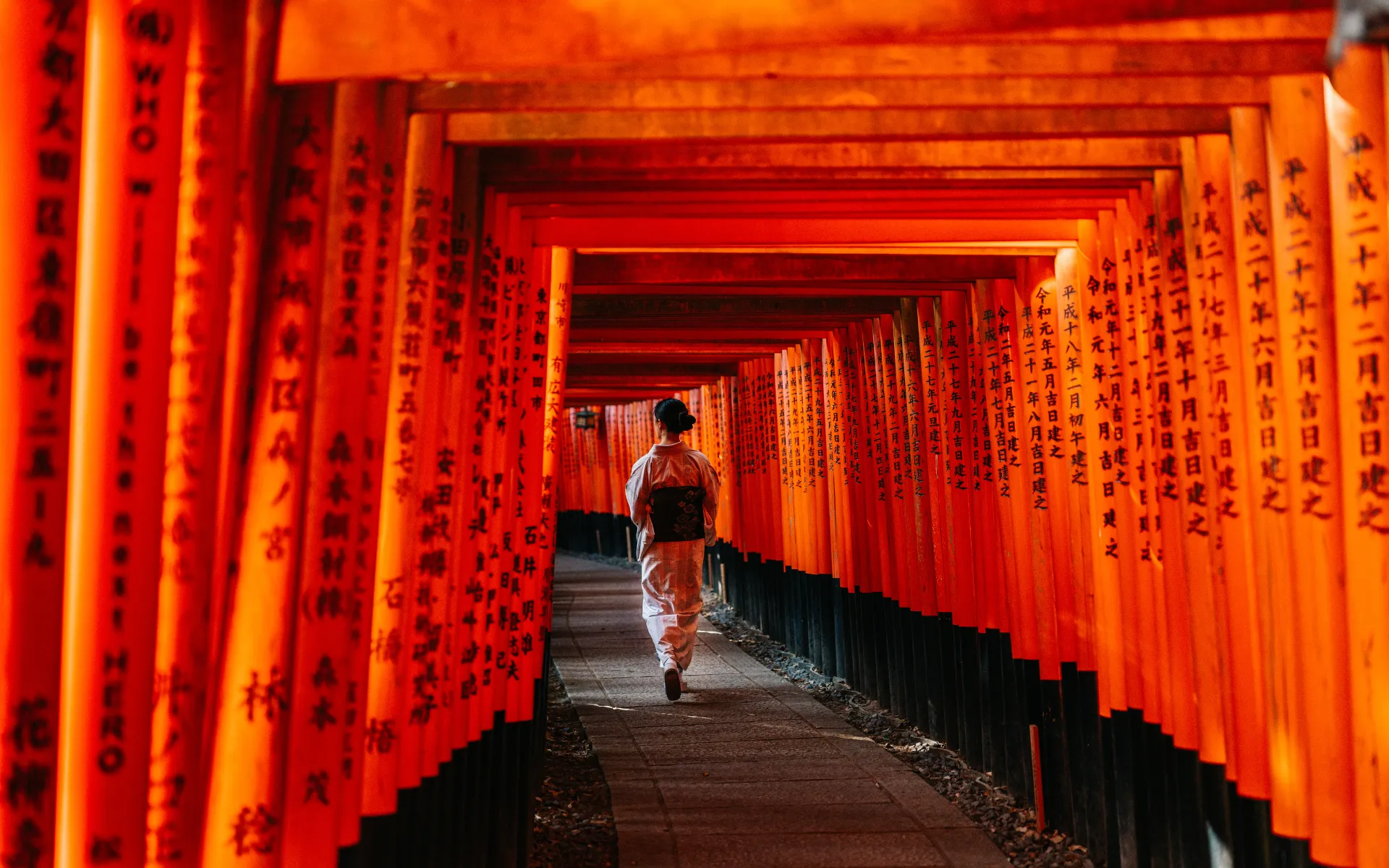 Person in traditional kimono walking through vibrant red torii gates at Fushimi Inari Shrine, Kyoto.