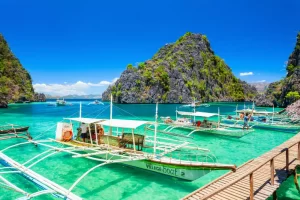 Stunning tropical landscape in Coron, Palawan, showcasing traditional bancas (outrigger boats) on brilliant turquoise water, surrounded by dramatic limestone formations under a clear blue sky, ideal for luxury group tours and exclusive MICE events.