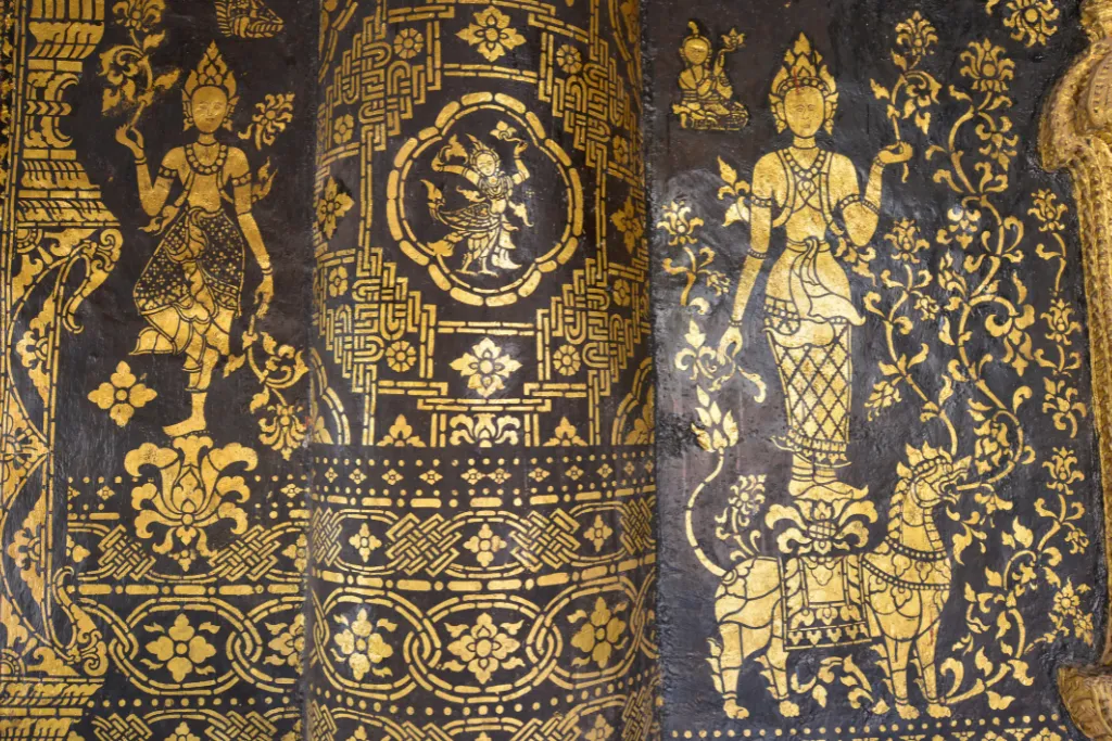 Intricate gold and black mural detail from a sacred temple in Luang Prabang, representing the rich cultural heritage of Laos, ideal for luxury cultural immersion.