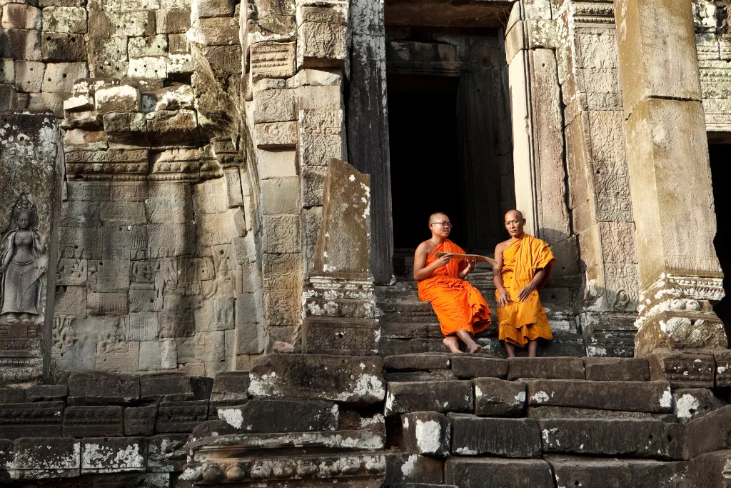 Two Buddhist monks at an ancient temple entrance in Angkor, depicting authentic cultural encounters for luxury travelers and bespoke tours arranged by a DMC.