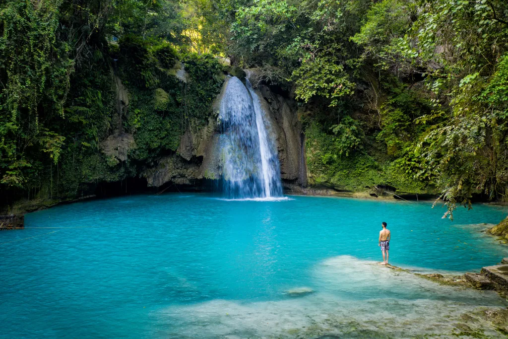 A solitary figure stands by the breathtaking turquoise pool of Kawasan Falls in Cebu, an iconic natural wonder perfect for luxury adventure tourism and exclusive group excursions.