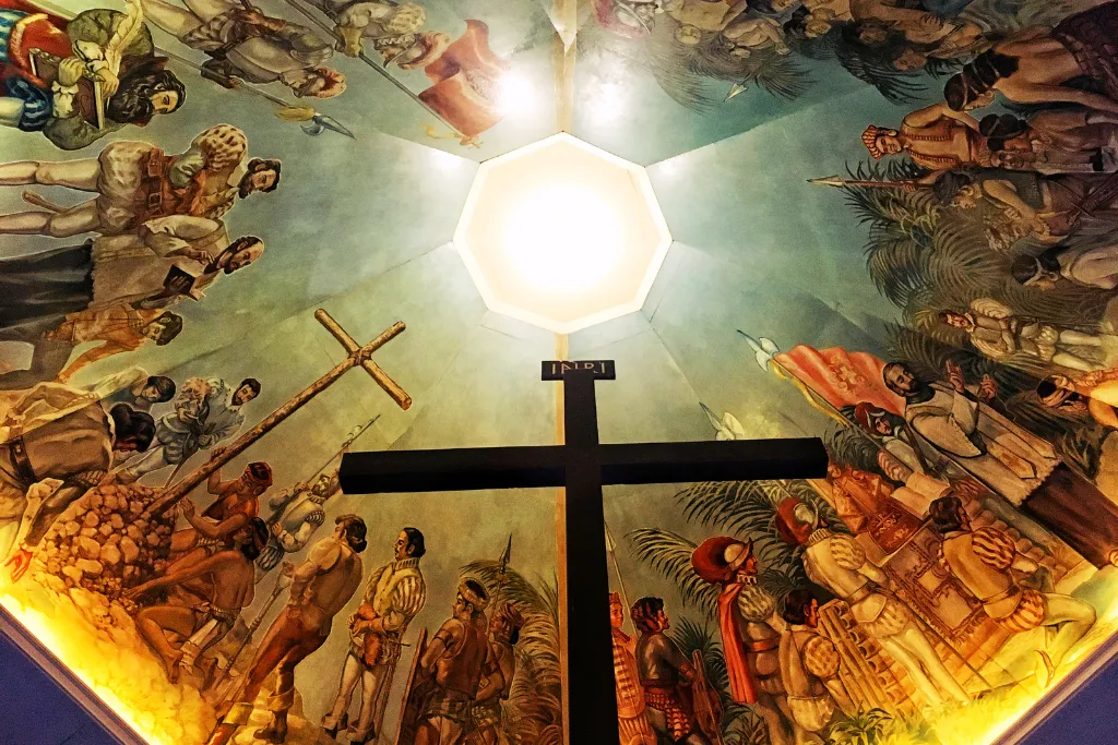 Intricate ceiling mural depicting historical scenes and a large cross within Magellan's Cross pavilion, offering a deep dive into Cebu's rich history for luxury cultural and MICE tours.