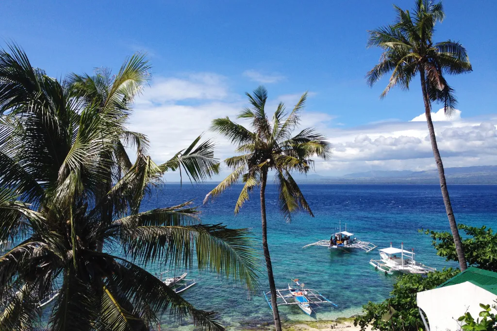 Stunning coastal vista in Dumaguete with vibrant blue waters, traditional boats, and lush palm trees. Perfect for luxury diving excursions, island hopping, and water-based team-building activities for MICE and DMC clients.