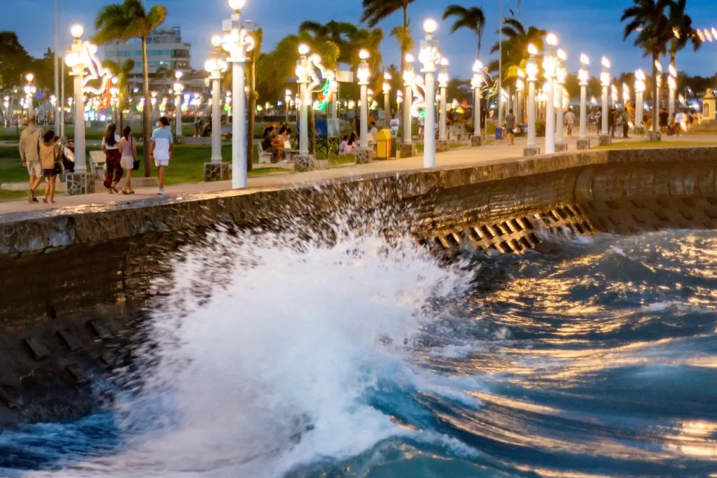Dynamic shot of waves crashing along Dumaguete's historic Rizal Boulevard at dusk, illuminated by charming streetlights. A perfect spot for evening strolls, waterfront dining, and exclusive events for luxury travelers and MICE groups.