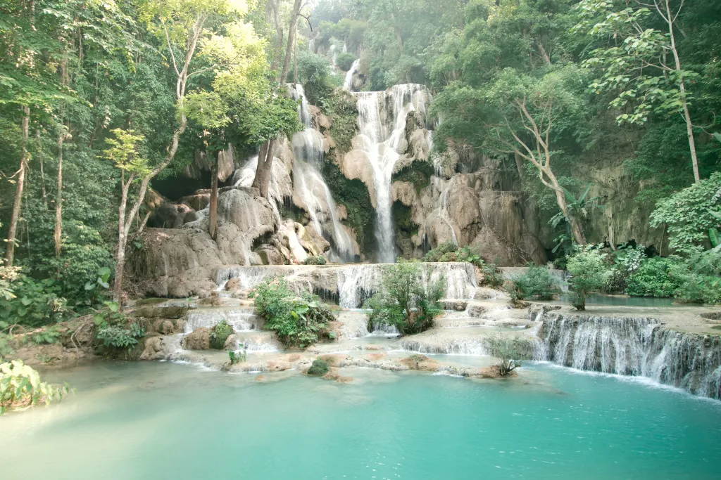 Majestic cascading tiers of Kuang Si Falls surrounded by lush jungle, a breathtaking natural attraction near Luang Prabang for luxury eco-tours and adventure travel.