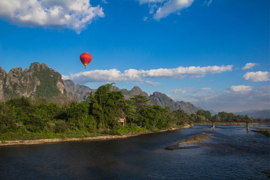 Red hot air balloon soaring above a scenic river and mountains in Laos, ideal for luxury incentive travel experiences and unique MICE activities.