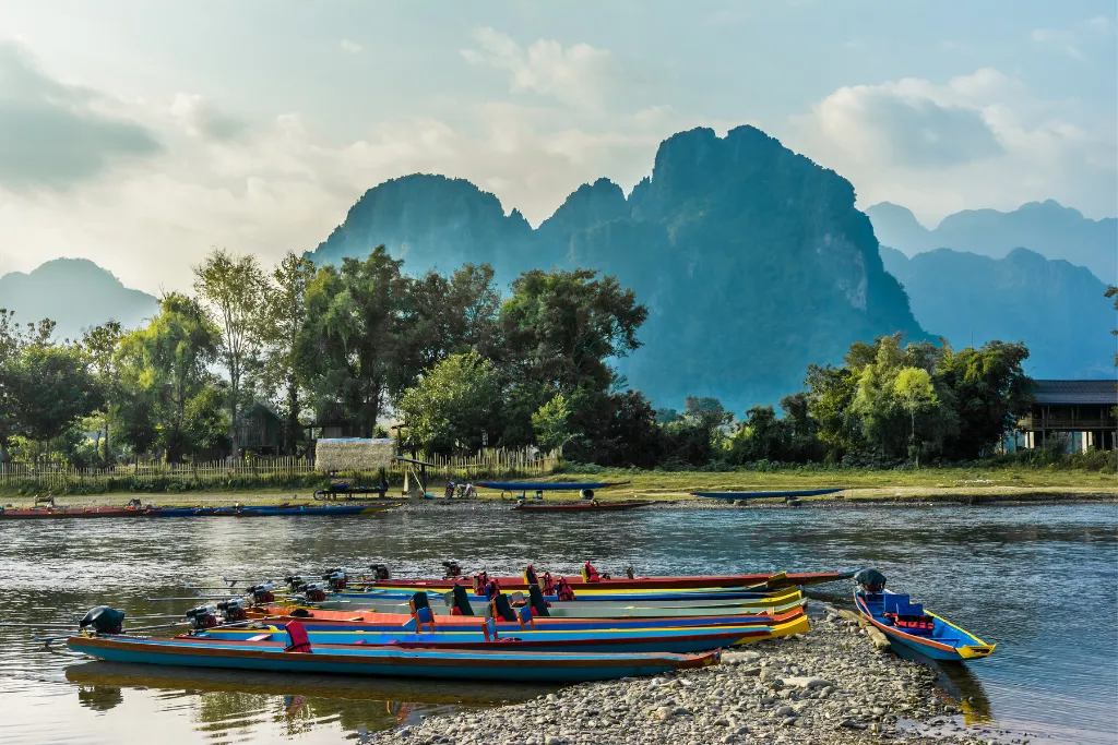 Colorful traditional longtail boats on a calm river in Laos, symbolizing bespoke river tours and luxury expeditions for discerning travelers.