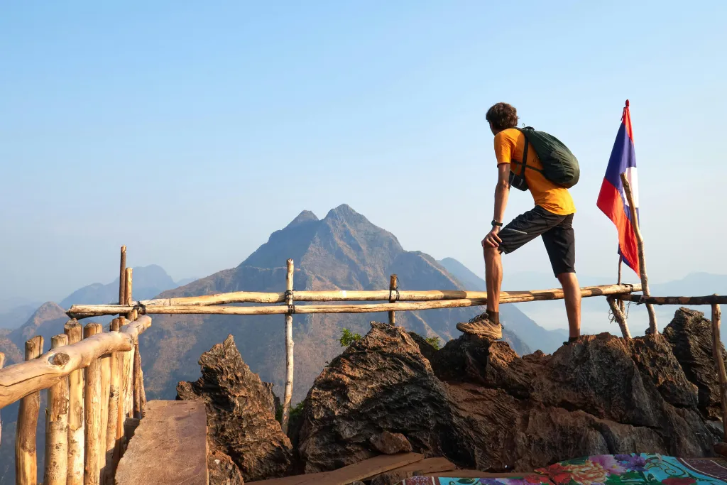 Adventurous traveler at a mountain viewpoint in Laos overlooking a stunning landscape, symbolizing bespoke luxury adventure tours and team-building activities.