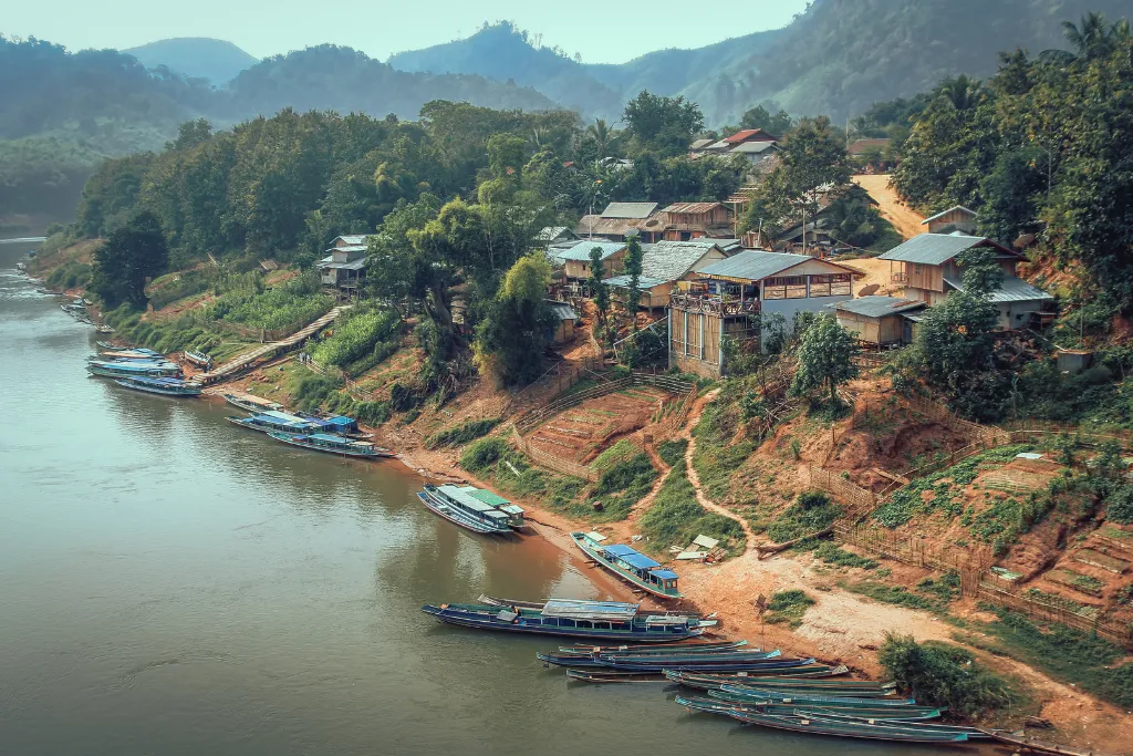 Charming riverside village in Laos with traditional boats docked, showcasing authentic local experiences and boutique accommodation options perfect for luxury travel and DMC services.