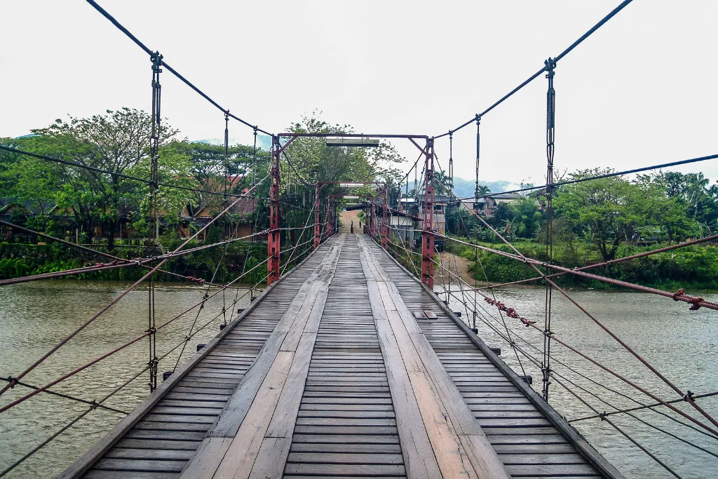 Rustic wooden suspension bridge over a river in Laos, showcasing adventure opportunities for luxury travelers and bespoke DMC itineraries.