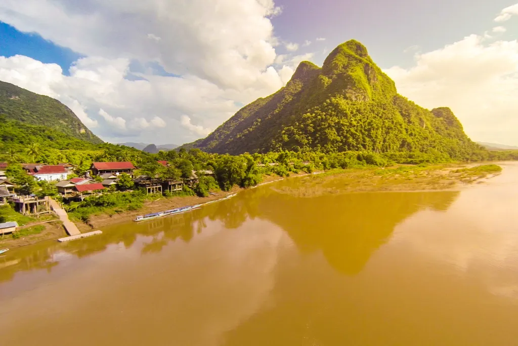 Aerial view of a serene Luang Prabang riverside village with lush mountains and the Mekong River, perfect for luxury Laos tours and MICE group experiences.