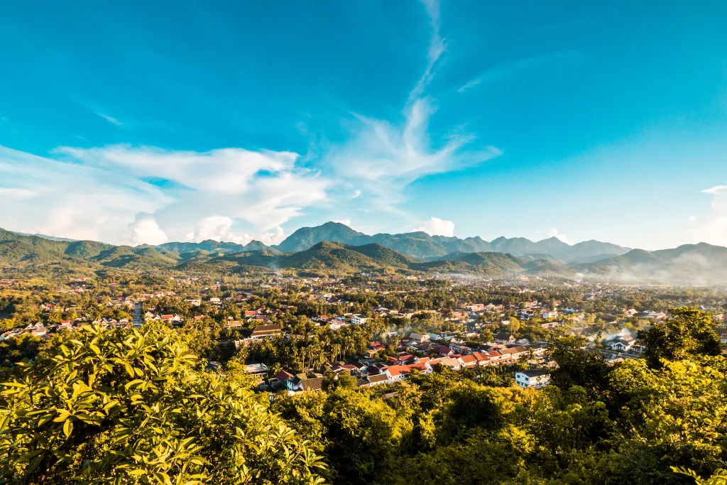 Breathtaking panoramic view of Luang Prabang city nestled amidst lush mountains under a vibrant sky, showcasing the beauty of this UNESCO World Heritage site for luxury group travel and DMC services.