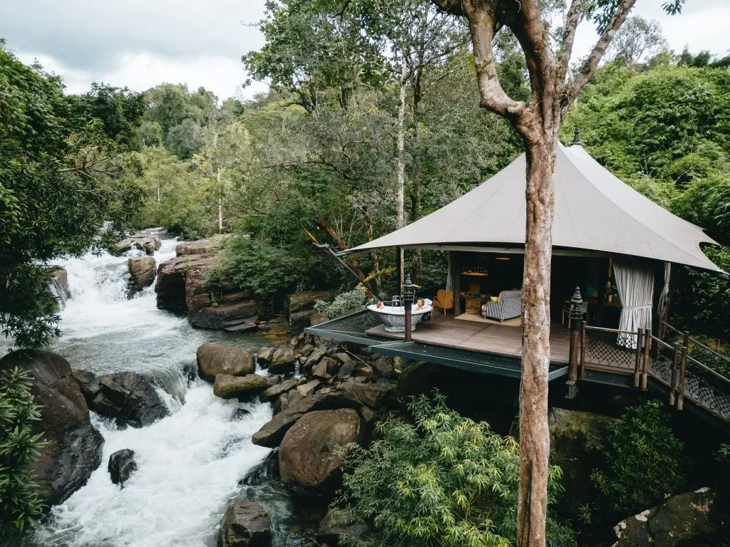 luxury-eco-resort-cambodia-waterfall-tent Luxury eco-friendly tented resort in a pristine jungle setting with a cascading waterfall, perfect for discerning travelers seeking unique experiences and sustainable luxury.