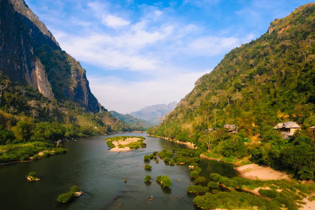 Aerial view of a serene river valley in Laos, flanked by lush green mountains and secluded luxury lodges, ideal for exclusive MICE events and private group retreats managed by a DMC.