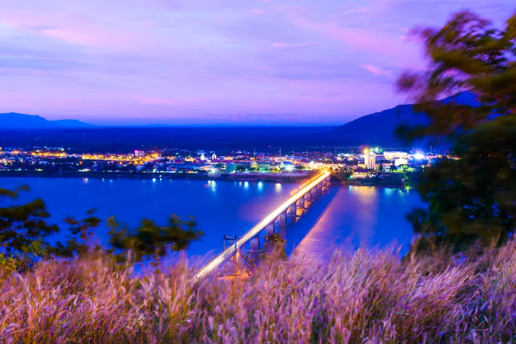 Luxury travel view of Pakse, Laos at night, showcasing the illuminated Mekong River bridge and city lights, ideal for bespoke itineraries and exclusive MICE events.