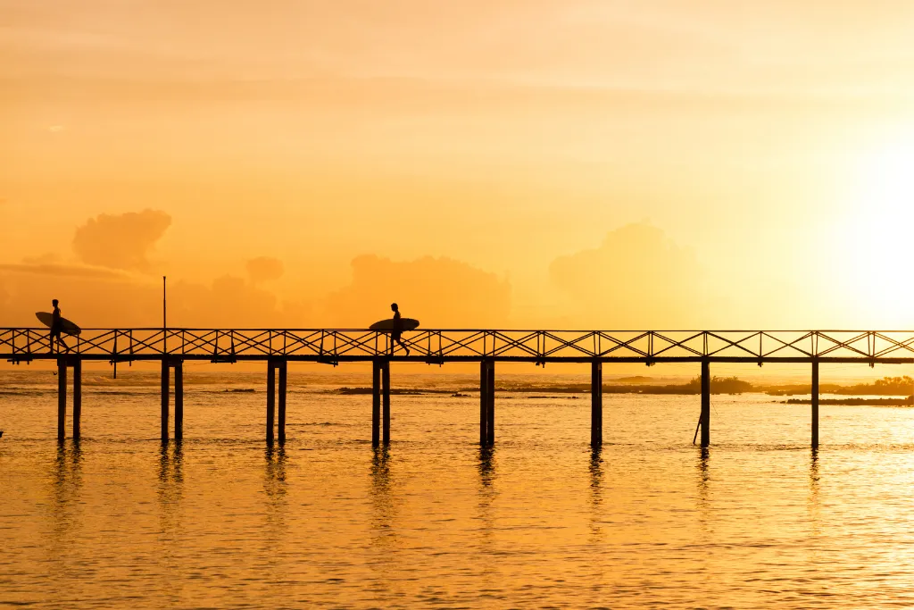 Silhouettes of surfers walking on a pier at sunrise in Siargao, signifying luxury surf adventures and exclusive morning activities for MICE and DMC itineraries in the Philippines.