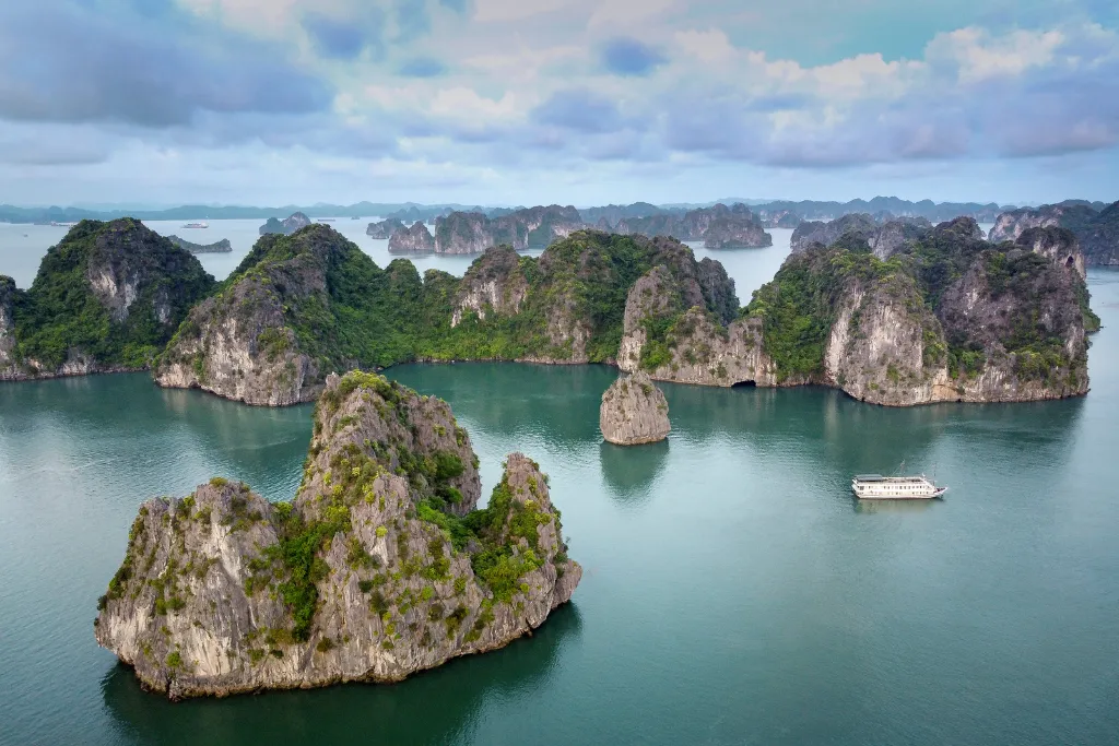 Expansive aerial view of Ha Long Bay's iconic limestone islands with a luxury cruise ship, ideal for large-scale MICE events and exclusive group voyages.