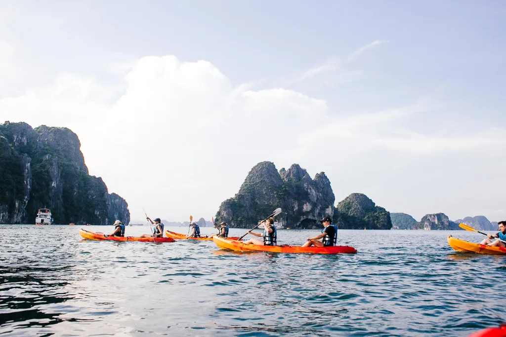 Guests enjoying kayaking amidst the karst islands of Ha Long Bay, a perfect adventurous activity for luxury tours and team-building MICE programs.
