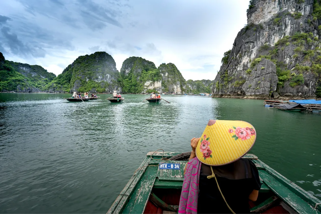 Traveler on a traditional boat enjoying the majestic karst landscapes of Ha Long Bay, highlighting the serene beauty for luxury and incentive travel.