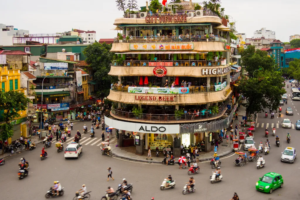 Panoramic view of a lively street intersection in Hanoi's Old Quarter with a multi-story cafe, showcasing the vibrant city life for luxury and MICE groups.
