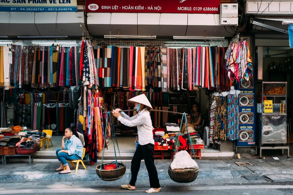 A traditional Vietnamese street vendor carrying goods in Hanoi's bustling market, embodying the authentic local culture for immersive luxury travel experiences.