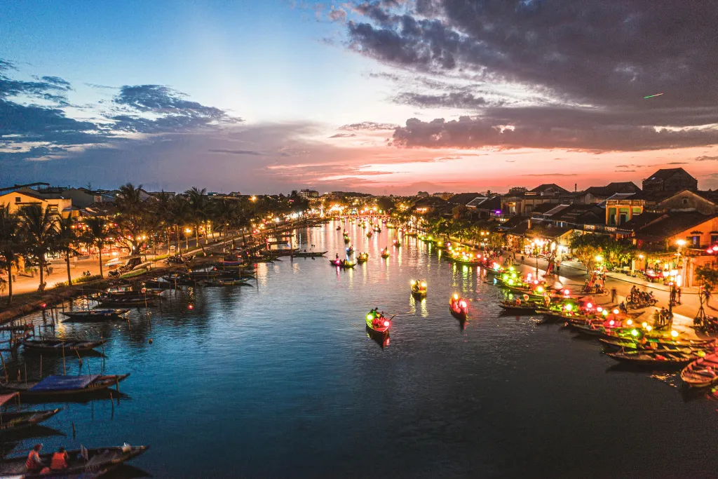 Enchanting night scene along the Thu Bon River in Hoi An, with illuminated boats and bustling riverside establishments, ideal for luxury evening events and MICE gatherings.