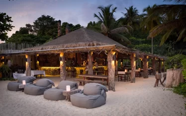 Elegant open-air beach bar and restaurant with lounge seating at dusk, perfect for exclusive events, private dinners, and group gatherings for MICE clients at a luxury private island resort.