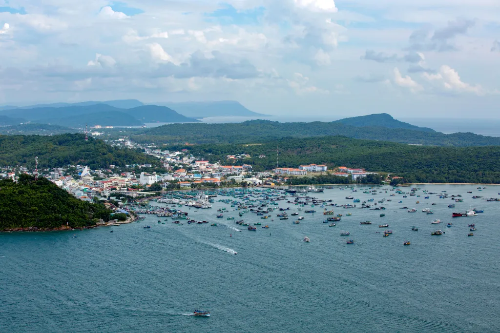 Aerial view of a bustling luxury harbor town in Phu Quoc, showcasing the vibrant fishing fleet and lush green hills, ideal for MICE and premium travel experiences.