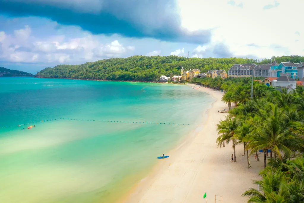 Breathtaking turquoise bay and pristine white sand beach in Phu Quoc, with upscale resort architecture in the background, showcasing an idyllic setting for luxury incentives and leisure travel.