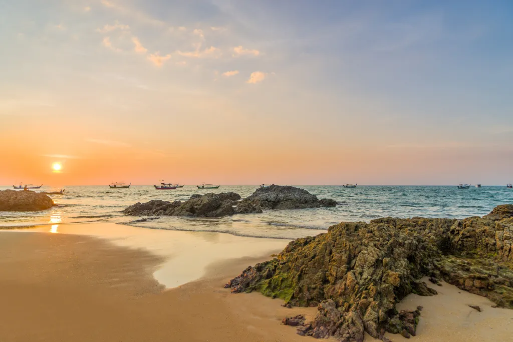 The stunning golden hour on a Thai beach, featuring local boats and a peaceful atmosphere, perfect for a corporate retreat or exclusive DMC tour.