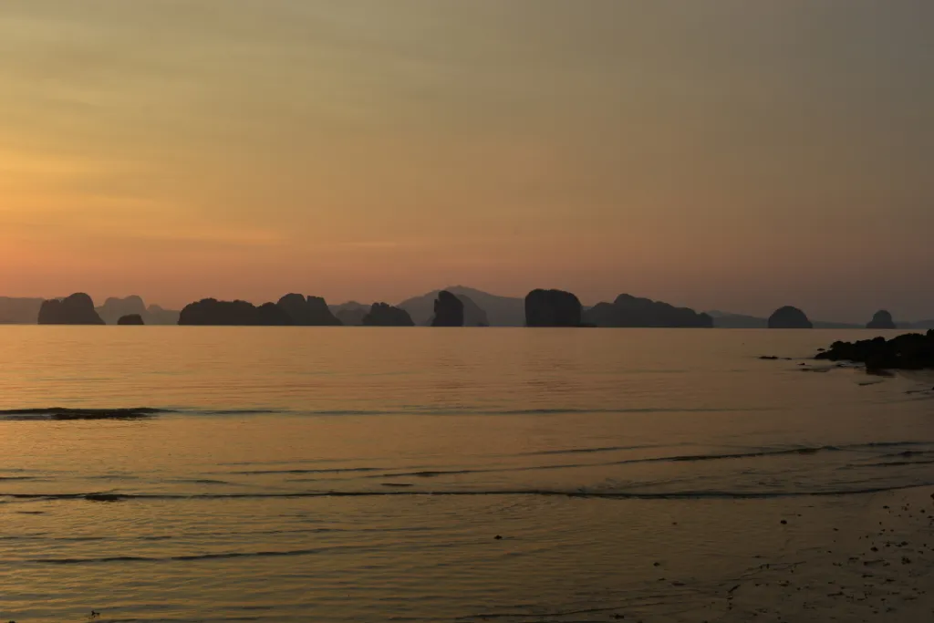 A stunning golden sunrise or sunset over the Andaman Sea with a silhouette of limestone karsts in the distance, showcasing a unique and luxurious backdrop for a MICE event or a DMC-planned corporate retreat in Thailand.
