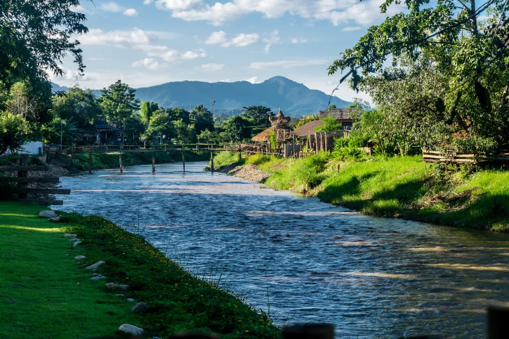A tranquil river flows through the lush, mountainous landscape of Pai, Thailand, showcasing the region's natural beauty. An ideal destination for a luxury escape or a DMC-curated itinerary.