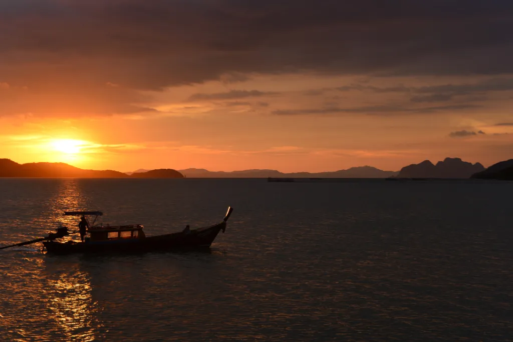 A stunning sunset view from a private long-tail boat in Thailand, showcasing the vibrant orange sky and serene ocean, ideal for a romantic or exclusive group tour.