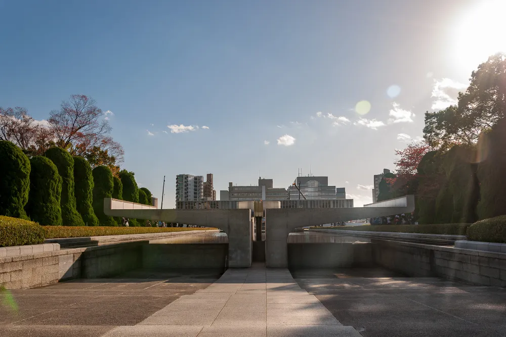 A serene view of the Hiroshima Peace Memorial Park, featuring the Cenotaph and surrounding tranquil landscaping under a clear sky.