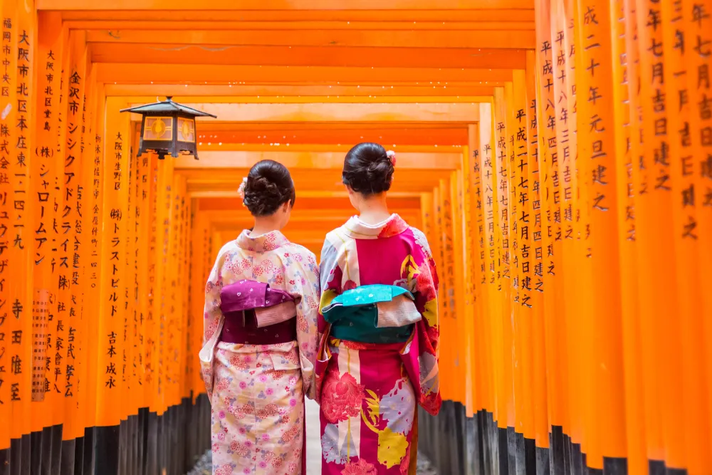 Two women in kimonos walking through the vibrant red torii gates of Fushimi Inari Shrine in Kyoto. This image highlights traditional culture and spiritual experiences on a luxury tour of Japan.