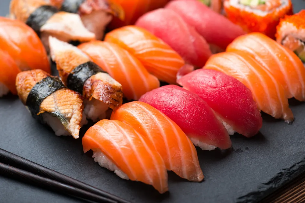 A close-up of beautifully arranged nigiri and maki sushi on a dark slate plate, with chopsticks on the side. This image highlights the premium culinary experiences of a luxury food tour in Japan.