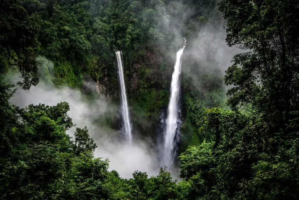Dramatic twin waterfalls plunging through the misty, lush green jungle of the Bolaven Plateau, Laos. Discover the natural beauty of the south on our custom Laos tours and adventure Laos holidays.