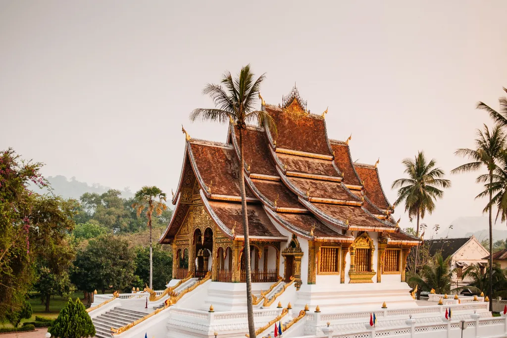The stunning golden facade and tiered roof of the Haw Pha Bang temple at the Royal Palace Museum in Luang Prabang, Laos. A key cultural highlight on bespoke Laos tours and luxury Laos holidays planned by our expert Laos DMC.