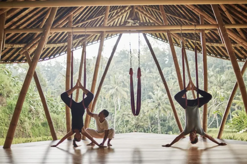 Guests enjoying aerial yoga in a beautiful bamboo pavilion in Ubud, symbolizing the ultimate Bali wellness and luxury travel experience. Perfect for rejuvenation on your custom-designed Indonesia holidays.