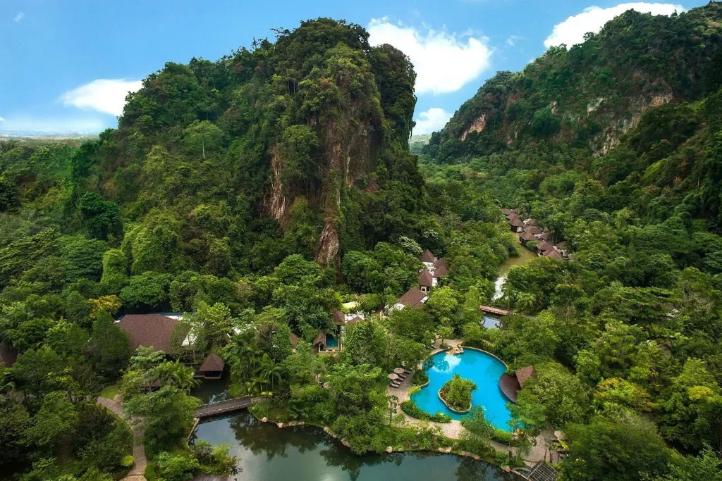 Aerial view of The Banjaran Hotsprings Retreat in Ipoh, Malaysia, showing the turquoise pool and villas surrounded by ancient limestone hills. Promote this secluded luxury wellness experience with our specialist Malaysia DMC tours and travel packages.